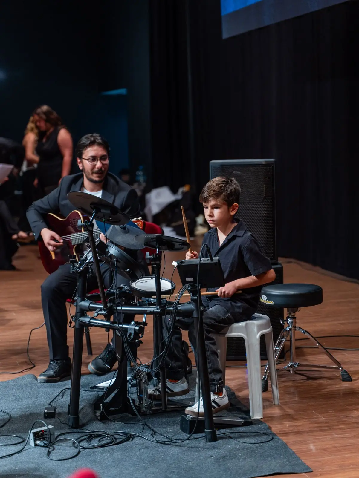 Elektronik bateri ve gitarla sahnedeki öğrenci topluluğu